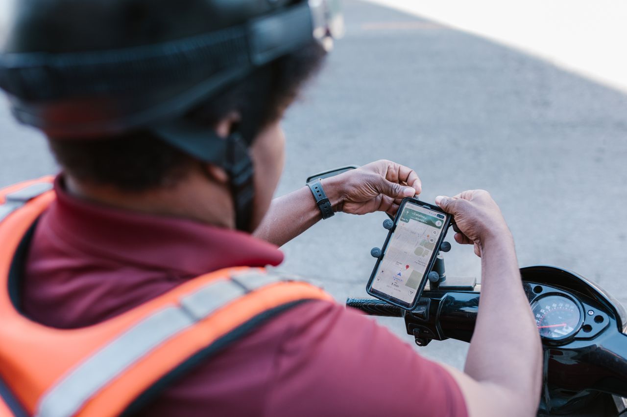services-02 A delivery rider checks directions on a smartphone mounted on a scooter outdoors.